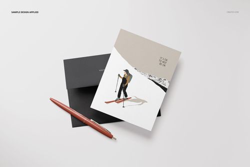 A2 card mockup with skier illustration and black envelope on a white surface, viewed from above with a pen nearby.