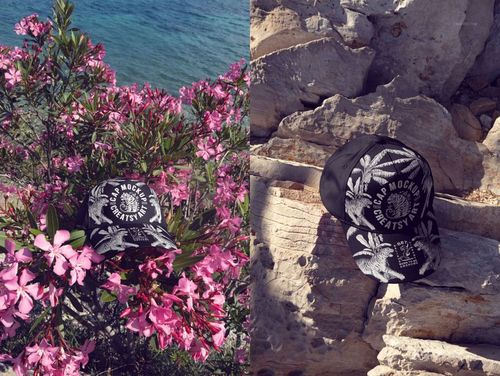 Classic snapback cap mockup displayed outdoors, with one cap among pink flowers and another on rocky terrain in sunlight.