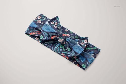 PSD mockup of a kids bow tie headband featuring blue and red bird and flower designs, displayed flat against a light surface.