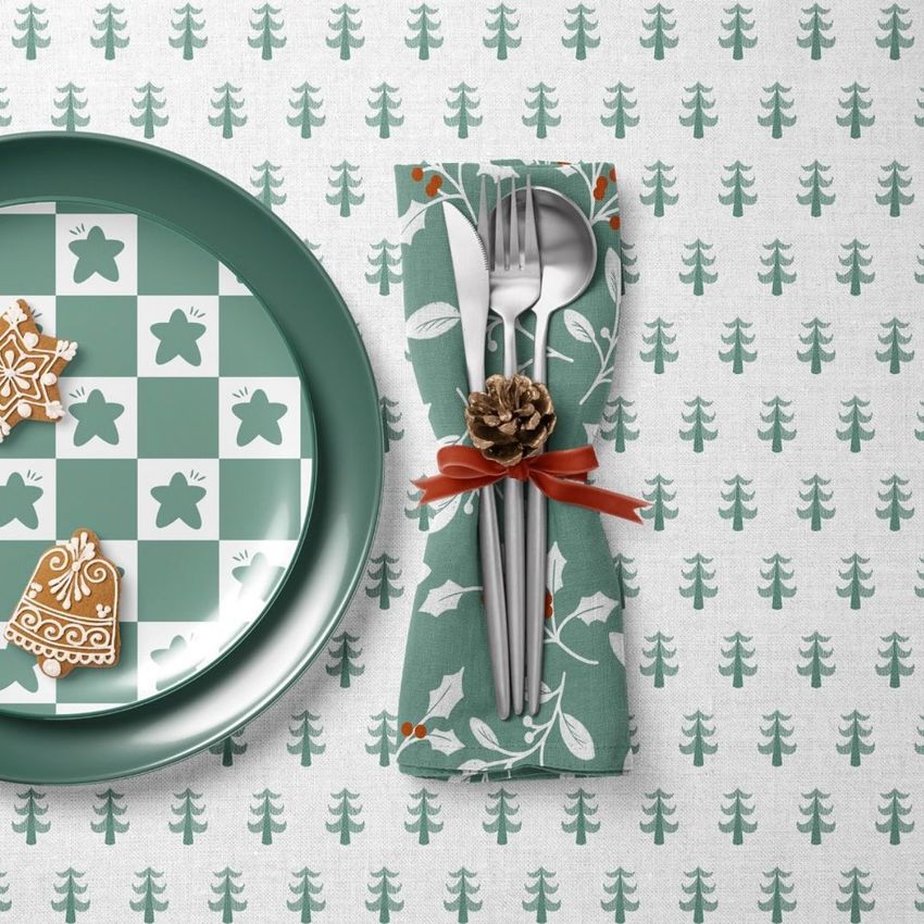 Plate, napkin, and tablecloth mockup featuring a green and white Christmas pattern with festive cookies and cutlery tied with a pinecone.