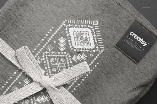 Close-up of a gray kitchen towel mockup featuring a white decorative design and a woven ribbon on a dark surface.