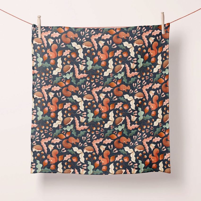 Crinkle muslin swaddle blanket mockup hanging on a line, featuring a colorful forest-inspired pattern with squirrels and leaves.