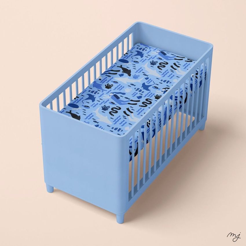 Crib sheet mockup featuring a blue crib with a patterned blue sheet, shown from an elevated angle on a light beige background.