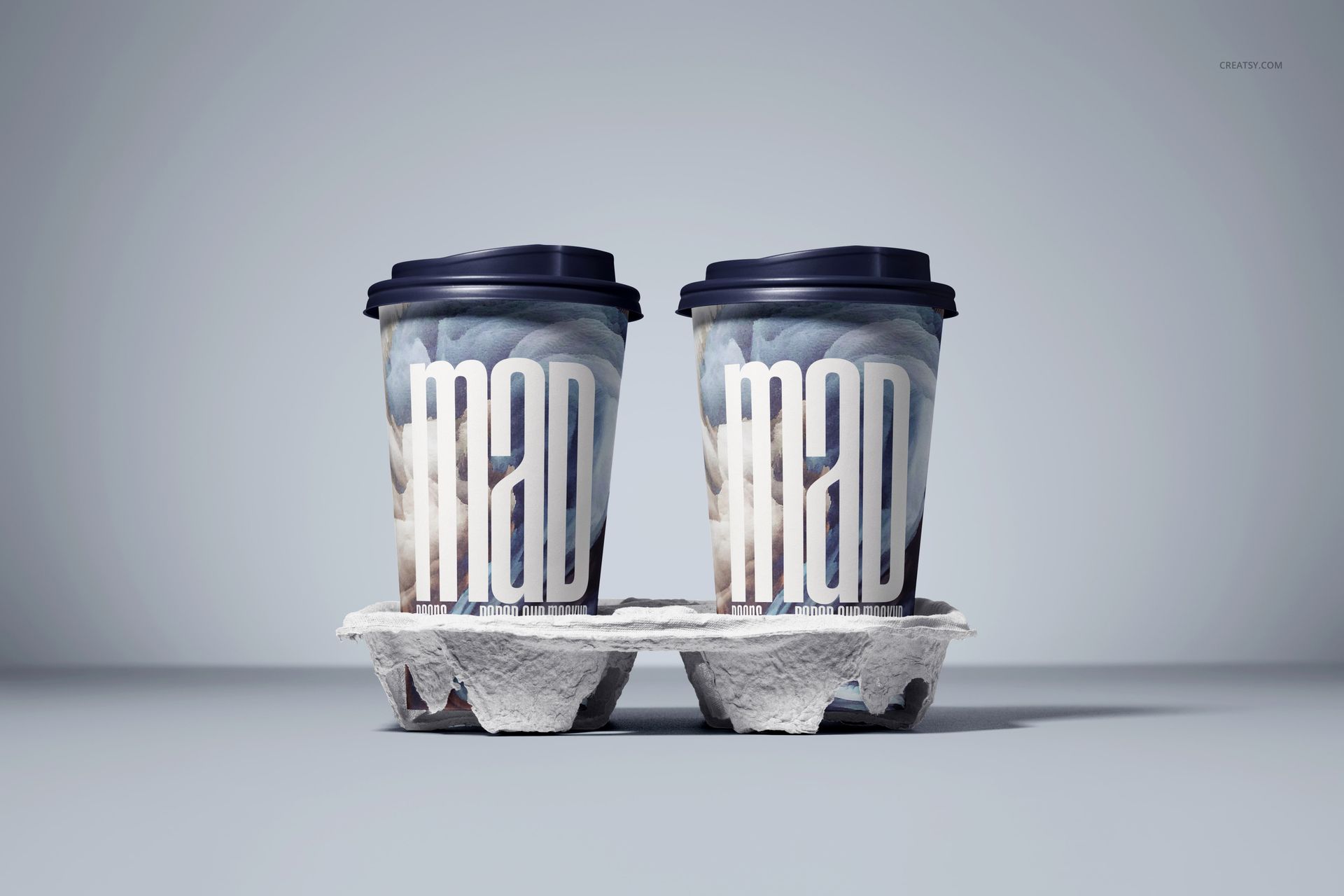 PSD mockup of two beverage cups with artistic patterns and lids, displayed in a gray cup holder against a light backdrop.