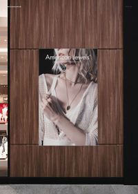 Vertical poster mockup displayed on a wooden wall near a store entrance, featuring a jewelry ad with a woman.