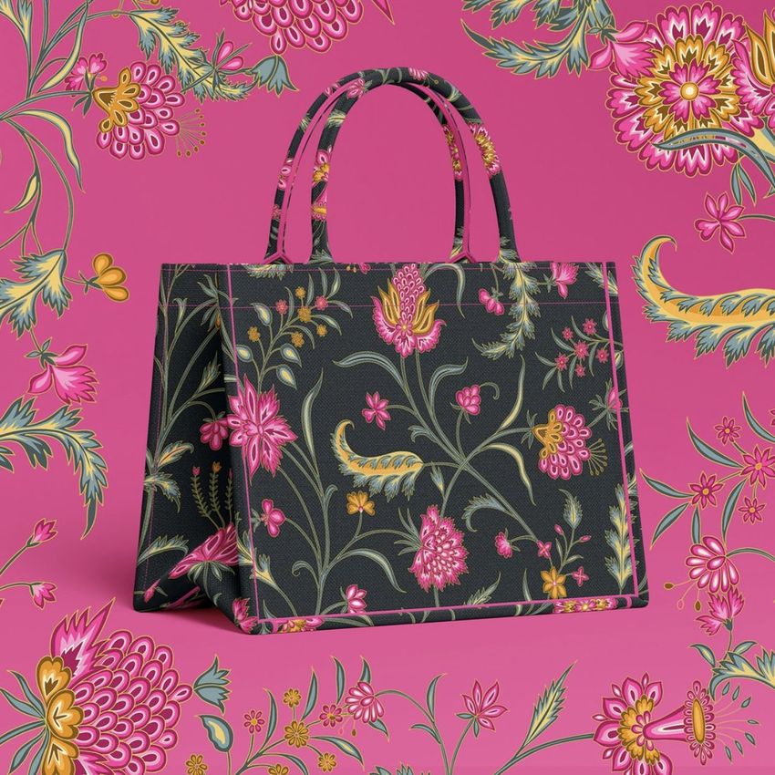 Canvas tote bag mockup featuring a dark bag with colorful floral patterns, set against a matching pink floral background.