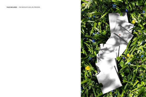 Stacked white fabric swatches with colored pins arranged on green meadow grass, top view, PSD mockup scene.