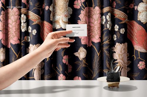 Front view of luxury fabric mockup featuring a dark background with pink and beige floral and bird motifs, hand and cup.