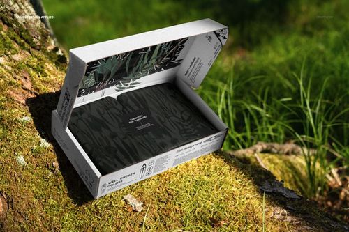 Open mailing box mockup with leafy print, placed outdoors on moss near tree trunk, sunlight highlighting textures.