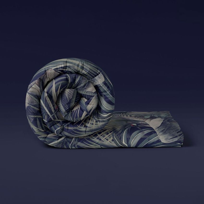 Rolled microfiber comforter mockup with a tropical leaf pattern in shades of green and blue on a dark background.
