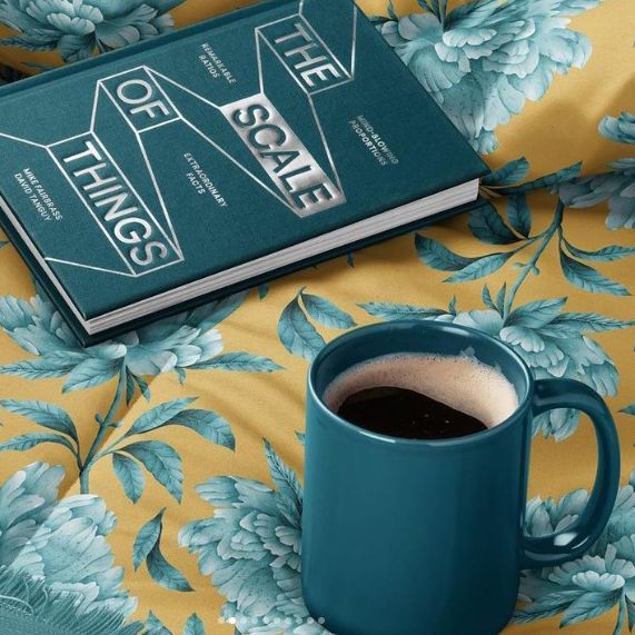 Microfiber comforter mockup featuring a yellow comforter with blue floral pattern, a teal book, and a teal coffee mug.