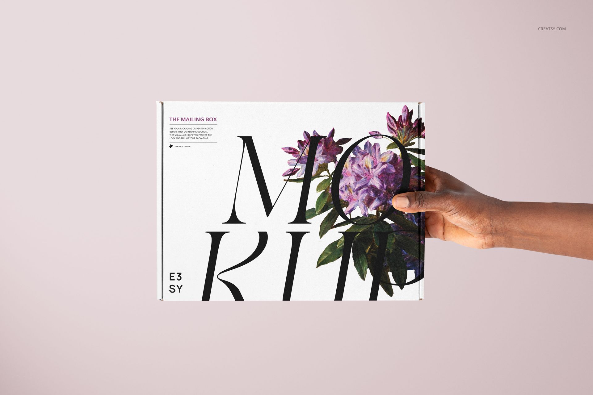 PSD mockup of a mailing box with floral graphics and black typography, presented in a person's hand on a pale backdrop.