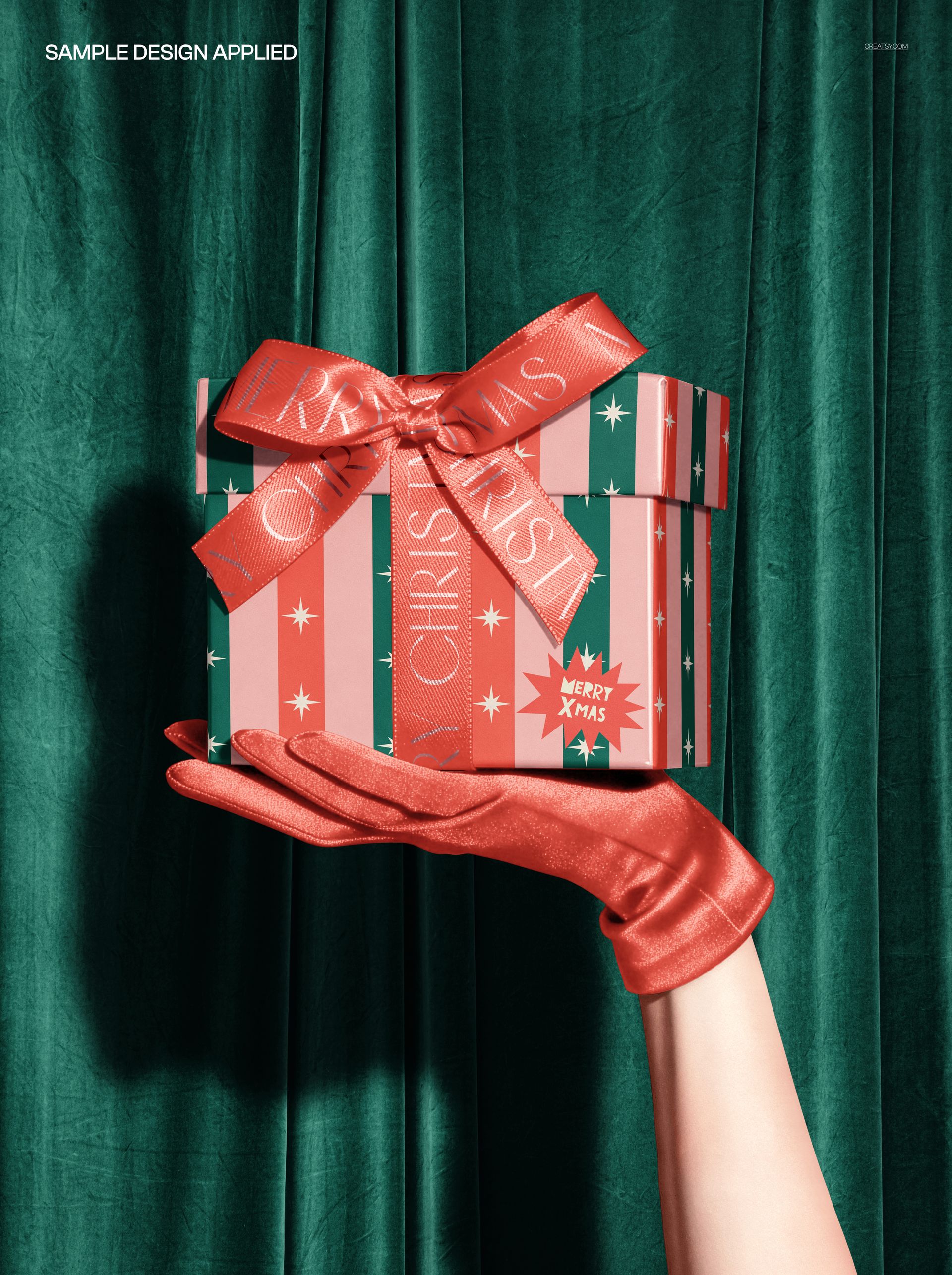 Christmas PSD mockup showing a hand in a shiny red glove holding a decorated gift box with bow, set against green drapes.