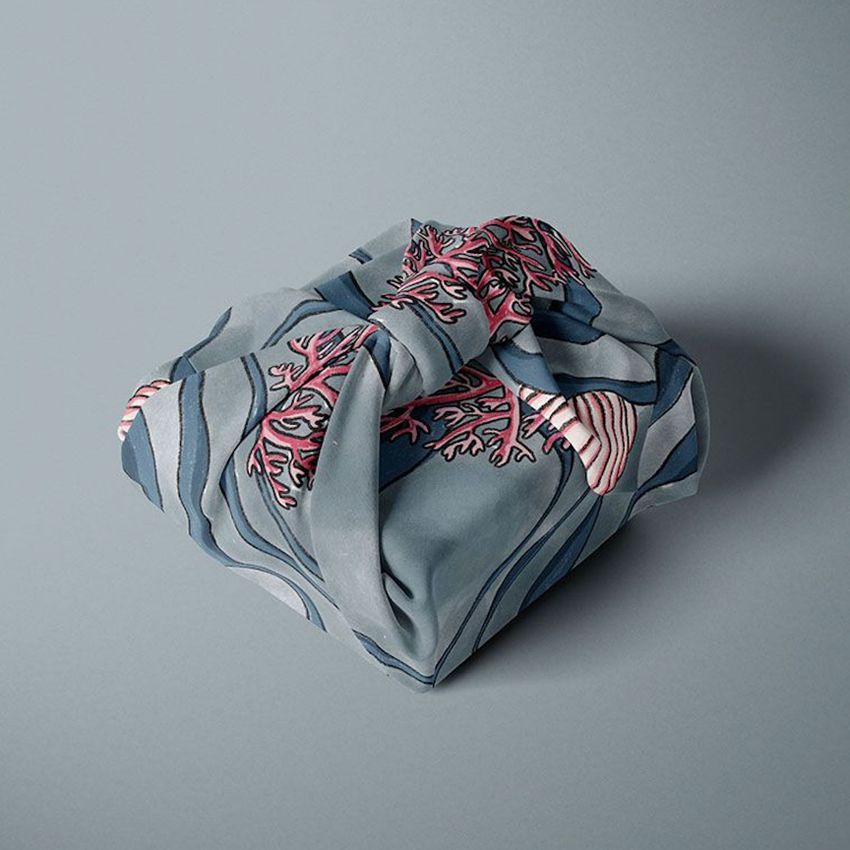 Fabric gift wrap mockup featuring a square package wrapped in blue cloth with pink and navy coral patterns on a gray background.