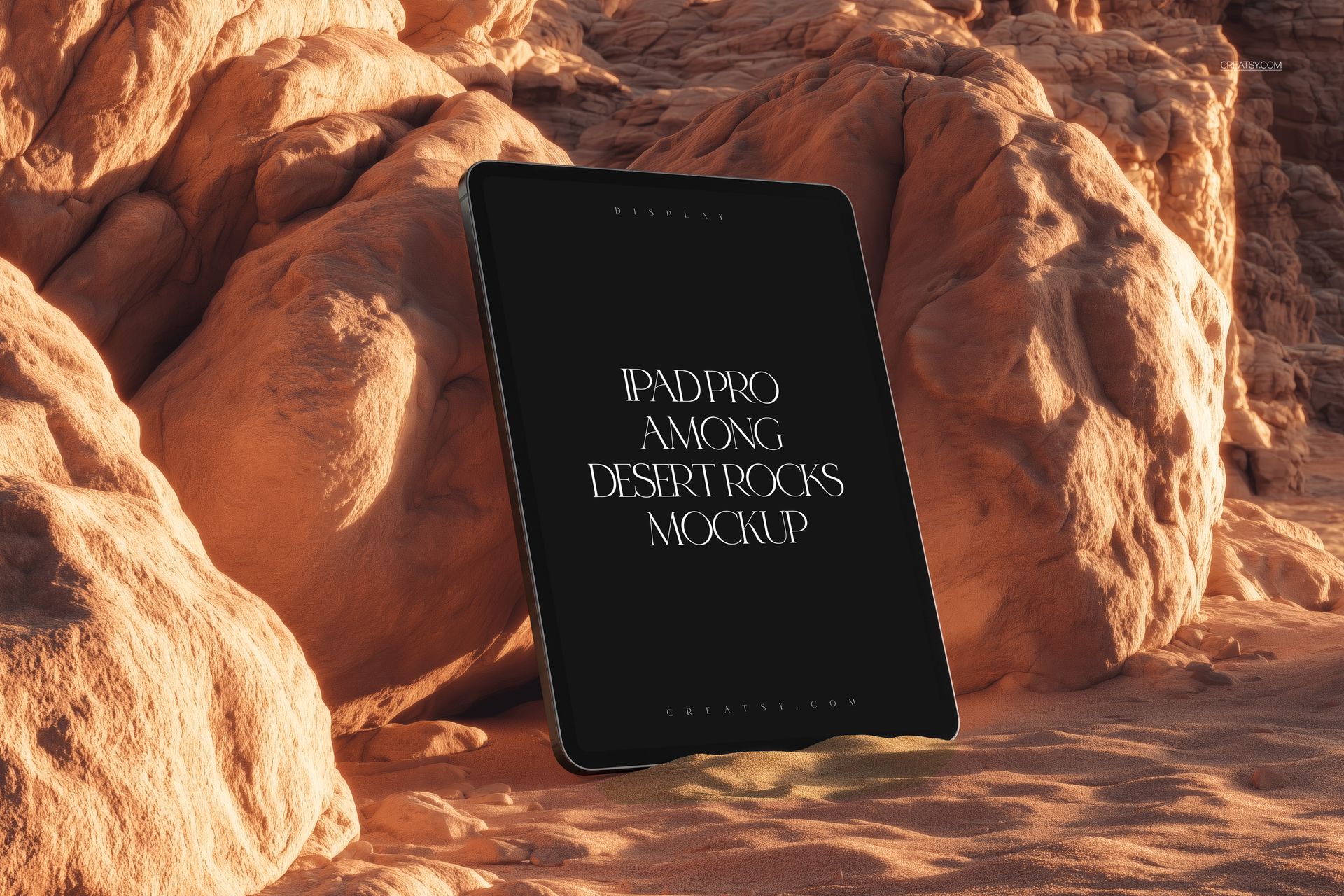 iPad Pro standing upright among textured desert rocks, black screen displaying mockup text, warm lighting.