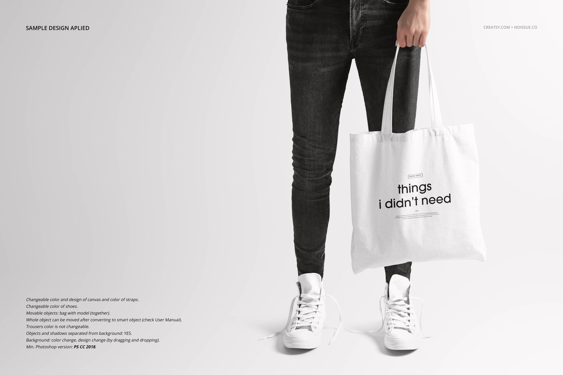 White tote bag mockup held by a person in black jeans and white sneakers, displayed on a neutral backdrop.