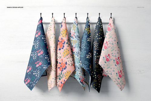 PSD mockup showing a row of tea towels with botanical prints in pastel and deep colors, suspended from hooks on a white background.