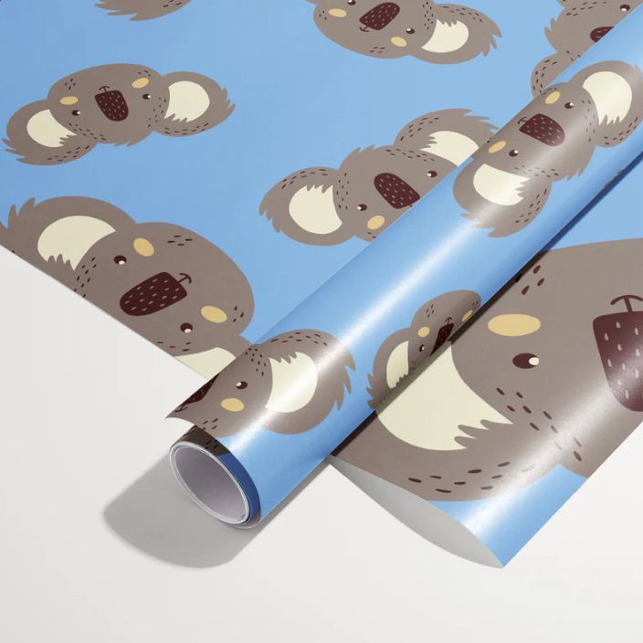 Gift wrapping paper mockup showing two rolled sheets with a repeating koala pattern on a blue background, photographed on a light surface.