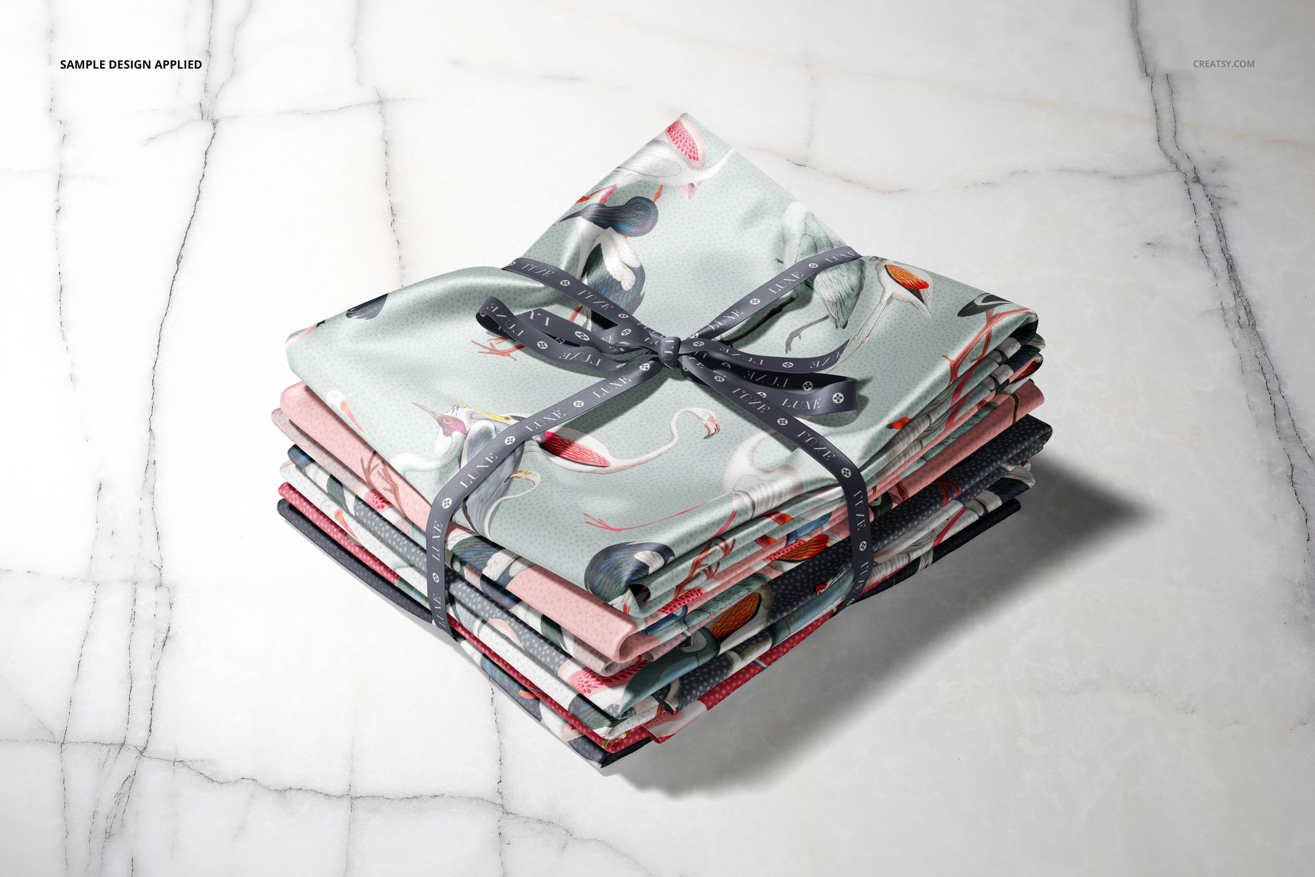 Satin fabric stack mockup featuring folded textiles in soft colors and floral prints, viewed from above on marble.