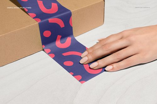 Noissue packing tape mockup showing a hand applying patterned tape to a cardboard box, top-down perspective.