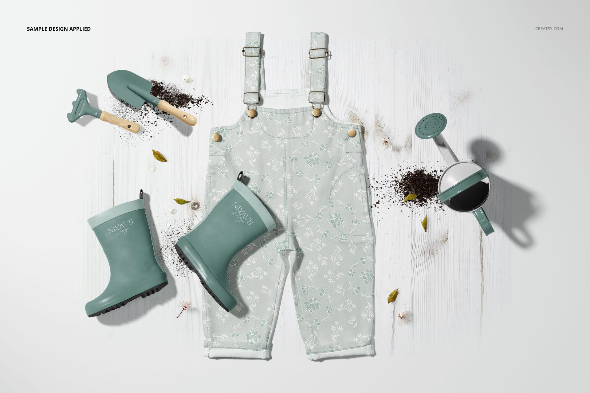 Children’s dungarees mockup with garden boots, spade, rake, and watering can, styled on a light wooden surface.