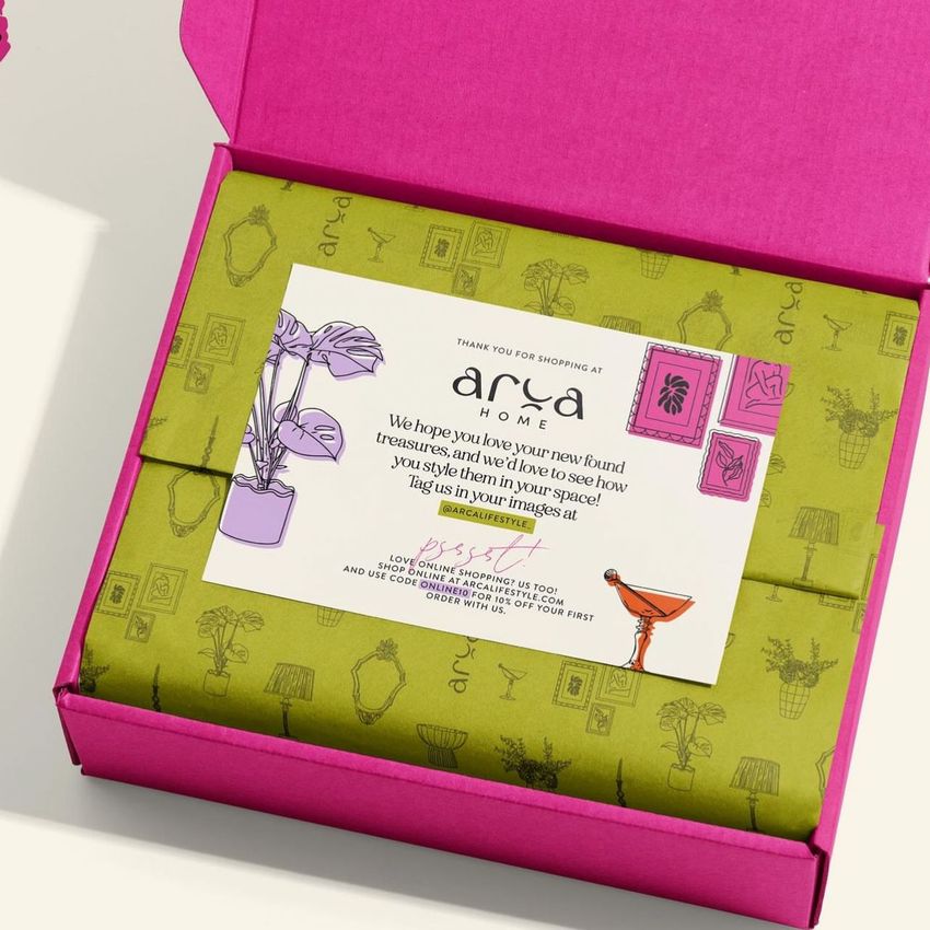 Stationery mockup showing a pink box with green patterned tissue paper and a printed card featuring text and illustrations.