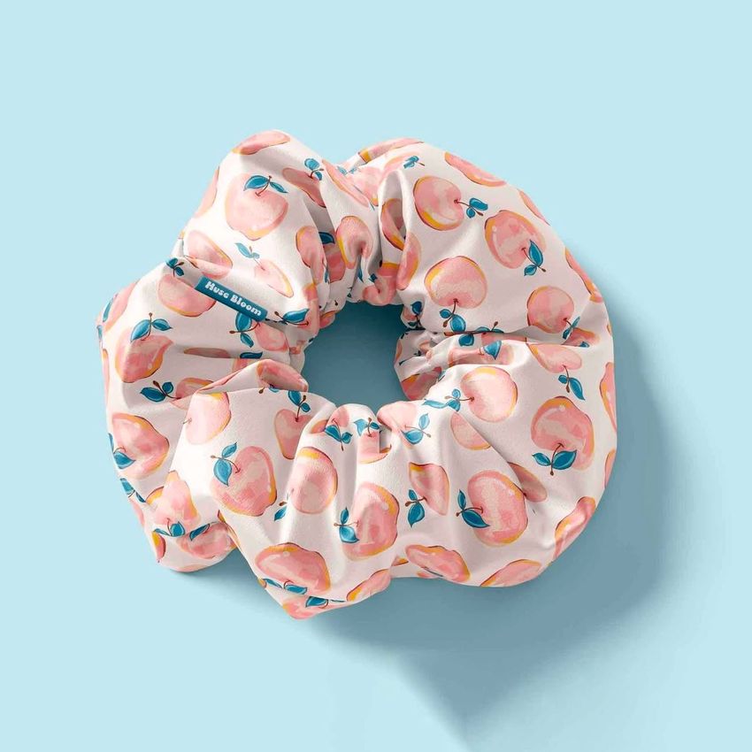 Hair scrunchie mockup featuring a fabric scrunchie with a peach fruit pattern on a light blue background, viewed from above.