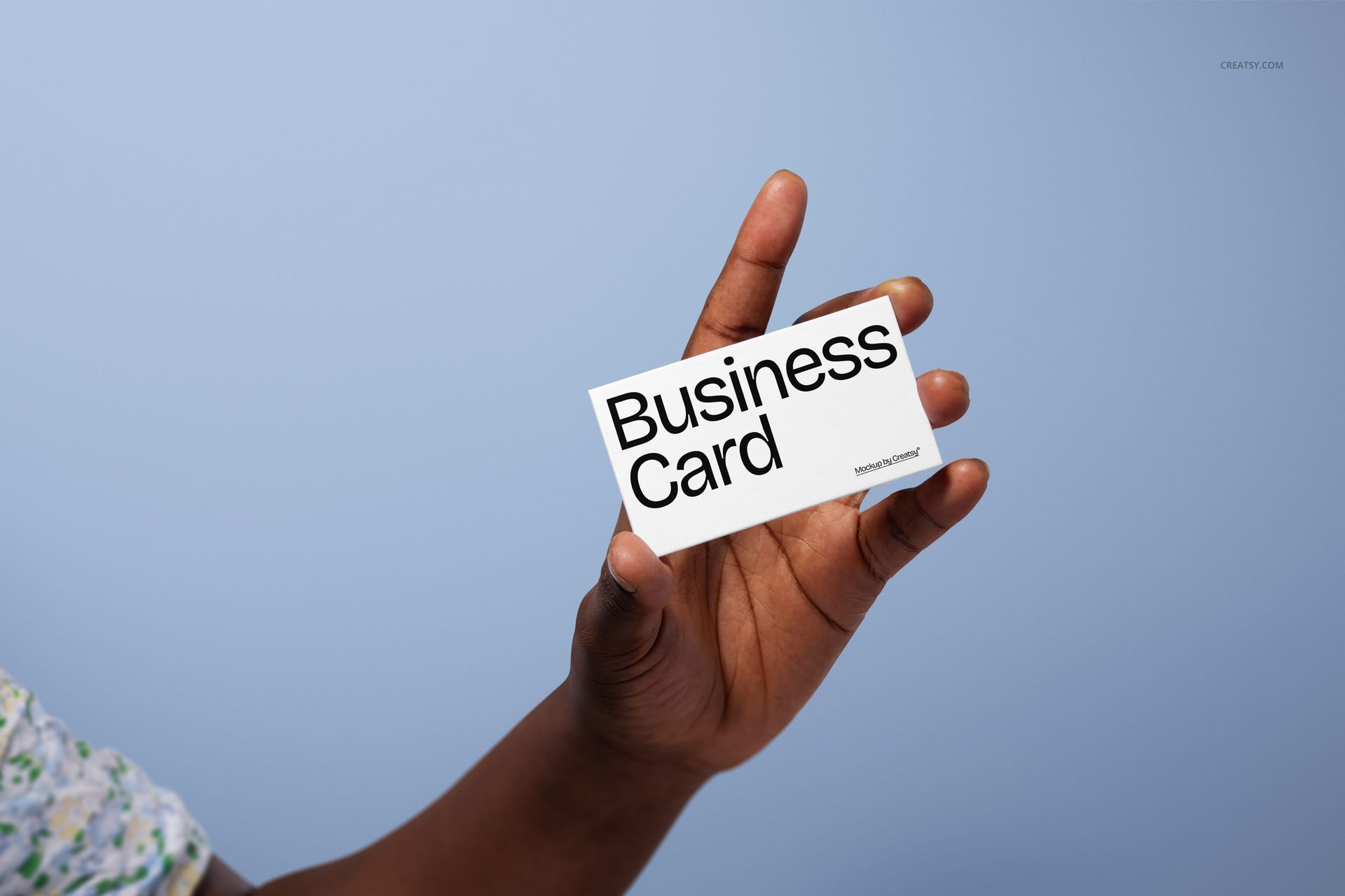 Business card mockup held between fingers of a female hand against a light blue background, close-up view.