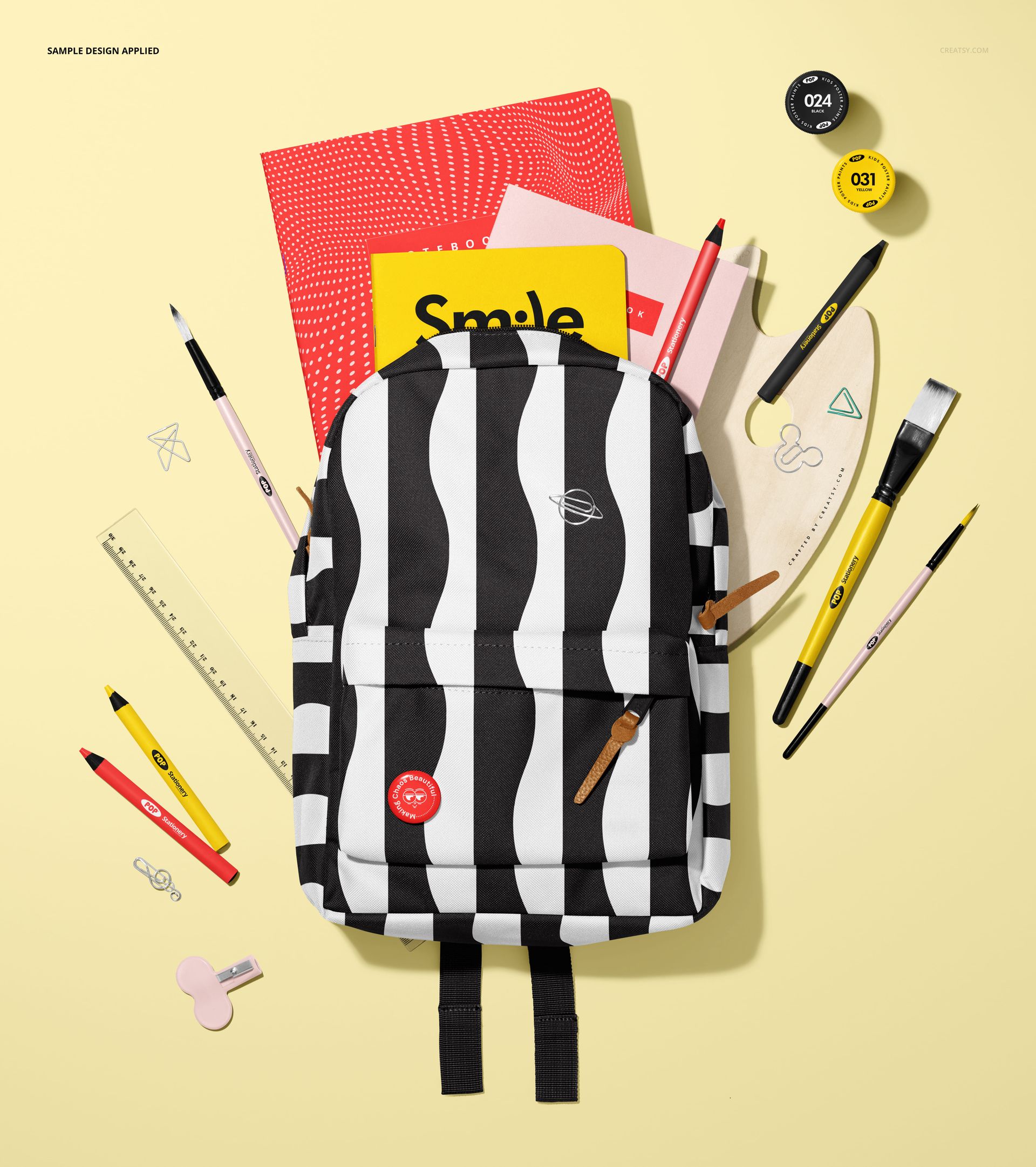 Black and white backpack mockup with various stationery items like notebooks, pens, and ruler arranged on yellow background.