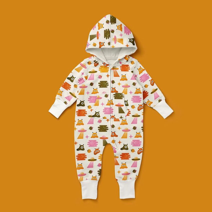 Baby fleece onesie mockup with a hood, featuring a colorful alien and UFO pattern on a white background, shown on an orange surface.