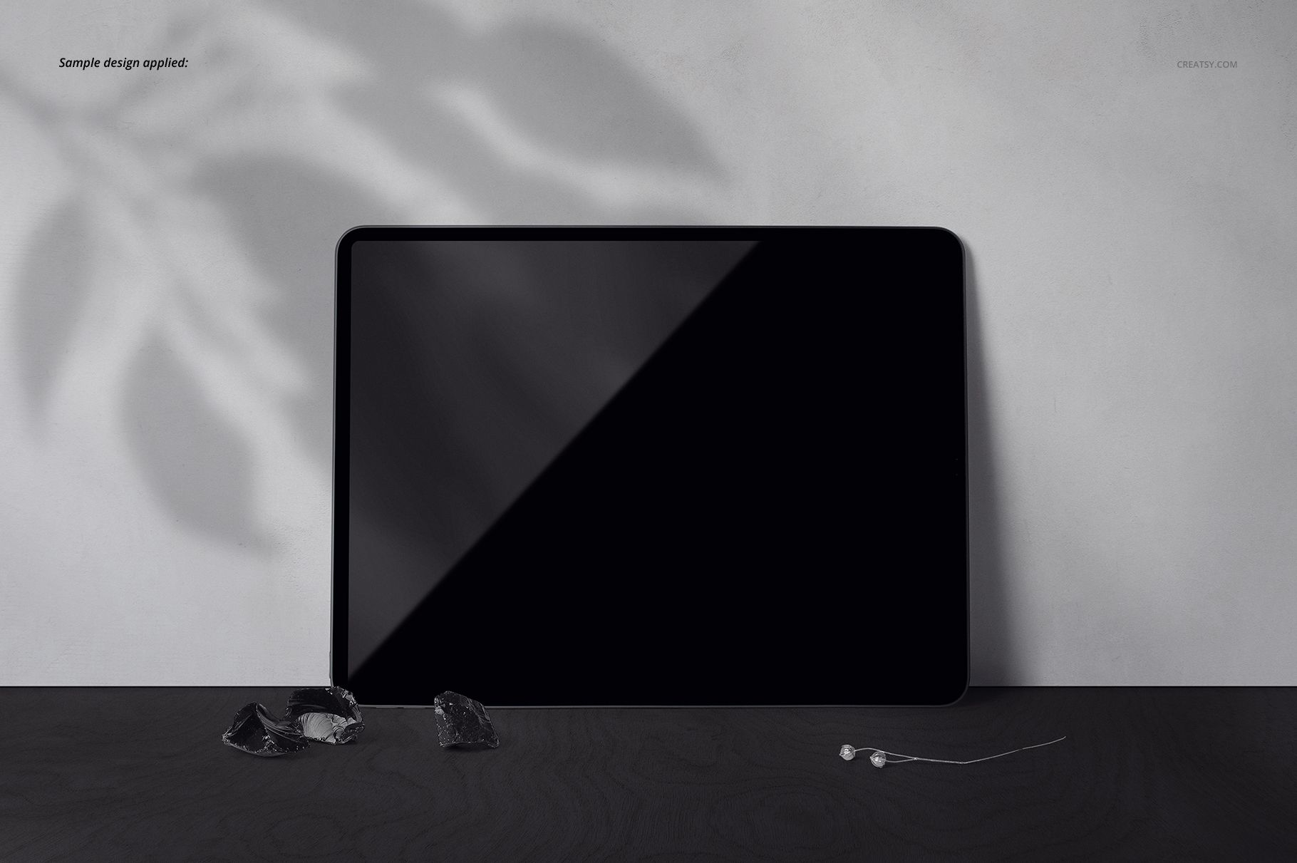 Black iPad Pro mockup displayed on a textured dark tabletop with a light gray background and scattered small objects.