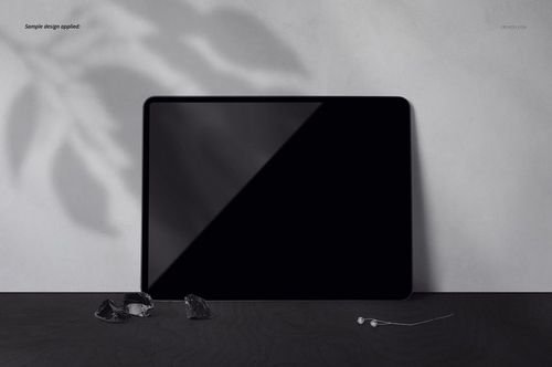 Black iPad Pro mockup displayed on a textured dark tabletop with a light gray background and scattered small objects.