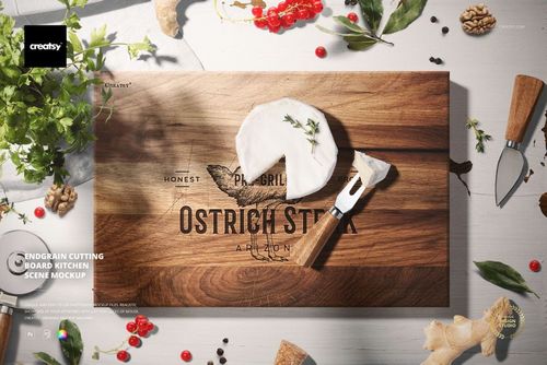 Top view of a wooden cutting board mockup with cheese, peeler, herbs, and kitchen utensils in a bright kitchen scene.