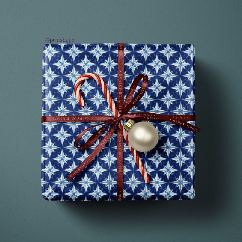 Christmas gift mockup featuring a blue patterned box tied with a brown ribbon, a candy cane, and a white ornament on a gray surface.