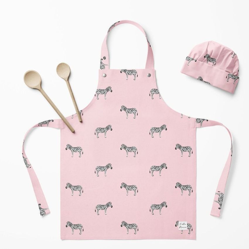 Kids apron mockup featuring a pink apron with a repeating zebra pattern, matching chef hat, and two wooden spoons on a white background.