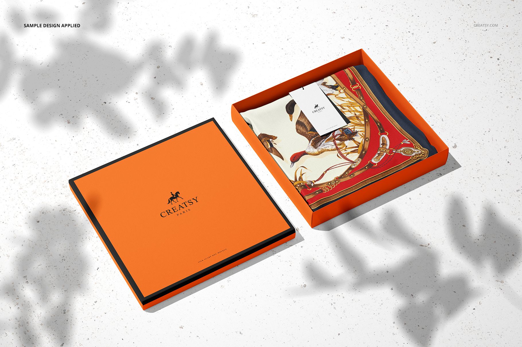 Open silk scarf box mockup set showing an orange square box with a patterned scarf and tag inside, top view.