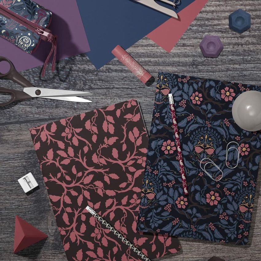 Stationery mockup featuring two classic A4 notebooks with floral covers, surrounded by pencils, scissors, and geometric props on a wooden surface.