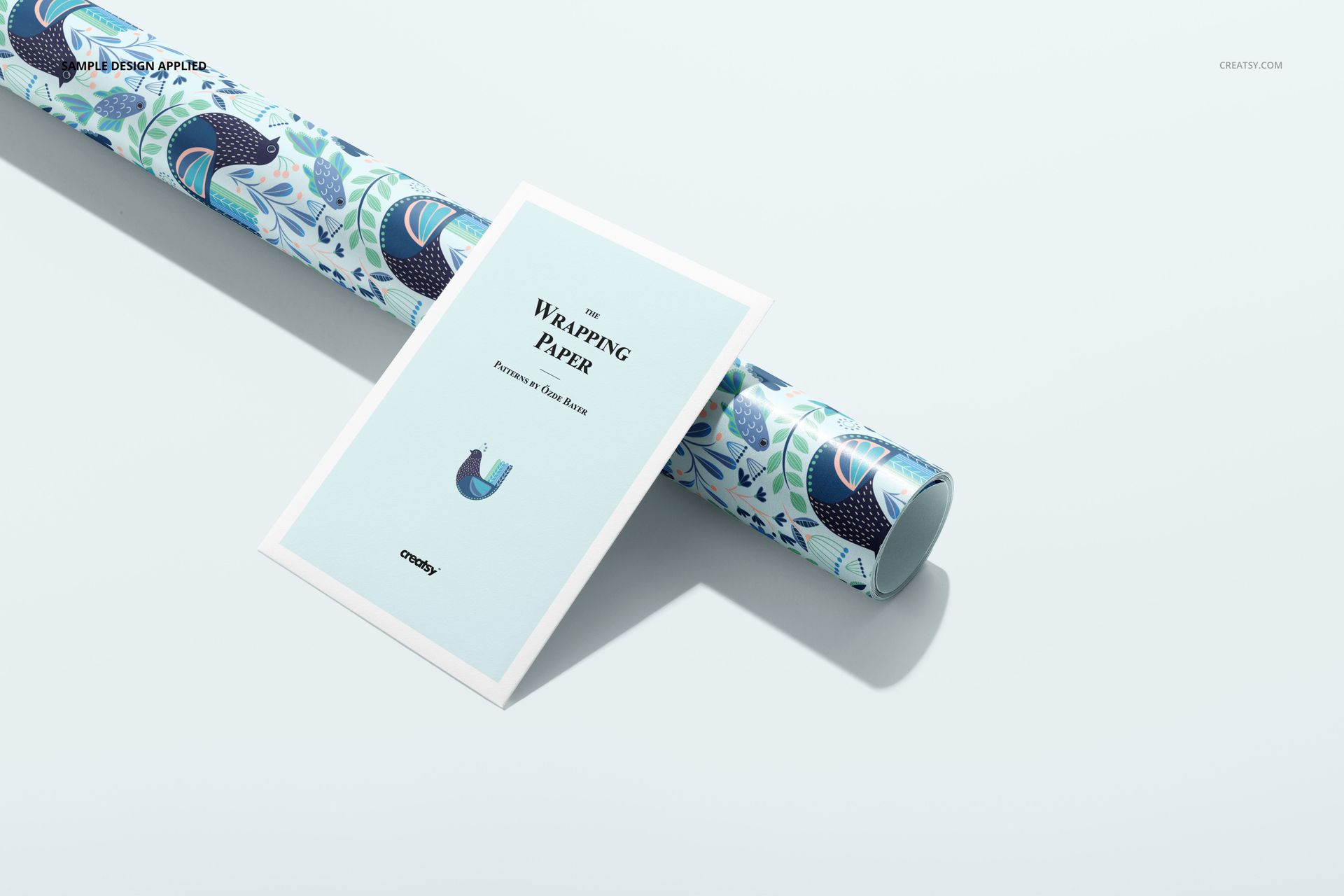 Gift wrapping paper mockup featuring a rolled sheet with a blue botanical design and a rectangular info card beside it.