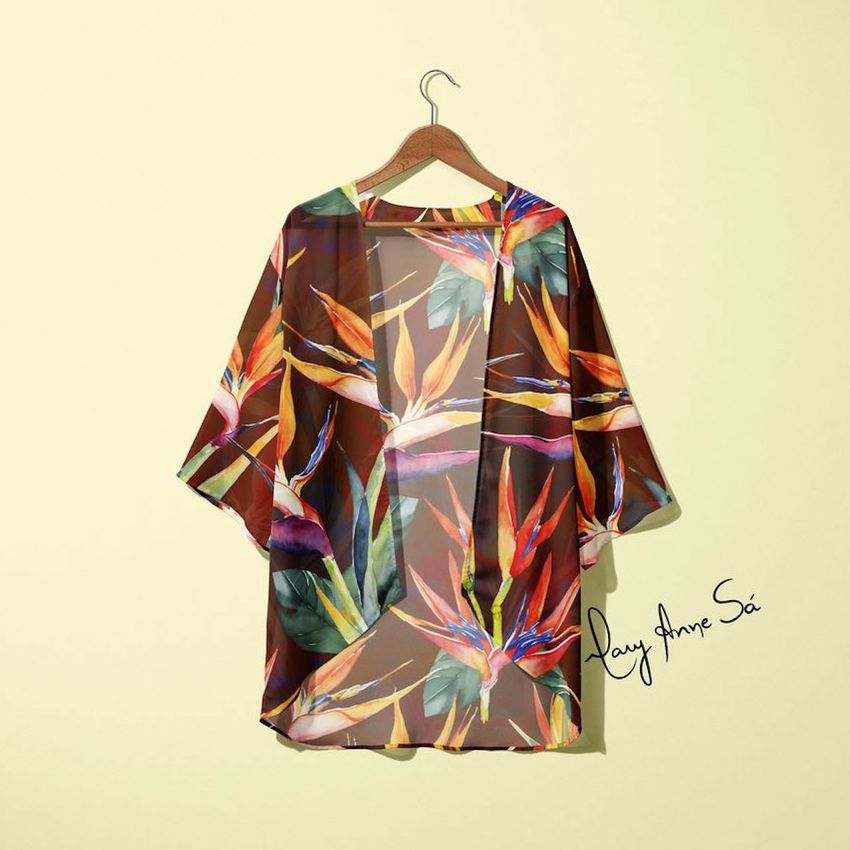 Chiffon kimono mockup hanging on a wooden hanger, featuring a colorful tropical bird of paradise floral pattern on a beige wall.