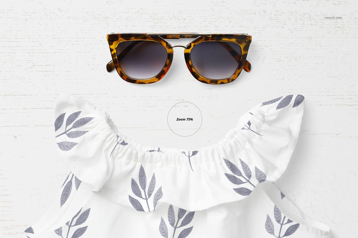 PSD mockup showing a baby summer outfit with leafy gray design and ruffled collar, paired with sunglasses on a light surface.