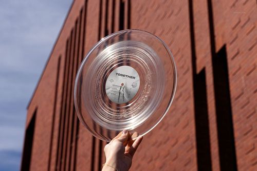 Transparent vinyl record mockup displayed outdoors, held up against a modern brick wall and sky.