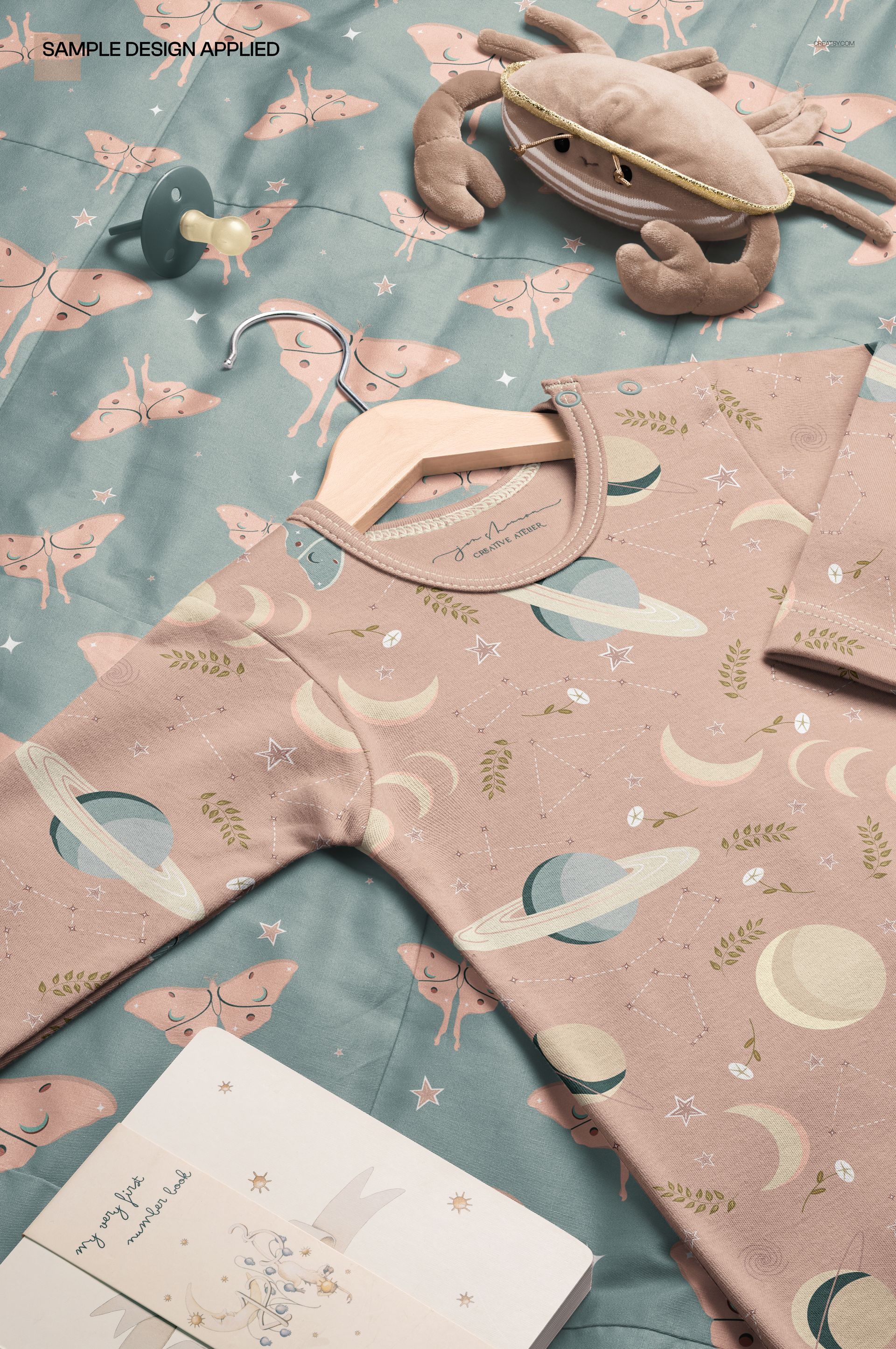 PSD mockup featuring a baby knotted gown in soft pink with celestial designs, laid out on a blue quilt with butterflies.