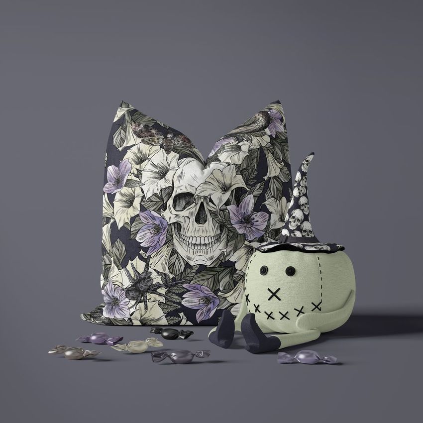 Halloween pillow mockup with a dark floral skull design, paired with a toy pumpkin wearing a witch hat on a gray background.