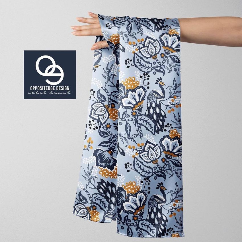 Silk scarf mockup draped over an outstretched hand, featuring a blue, white, and gold floral and peacock pattern.