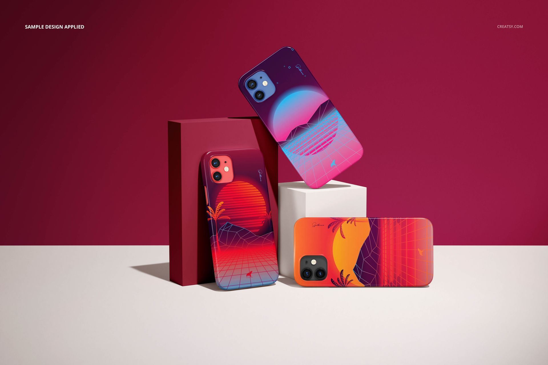 Glossy iPhone 12 mockup cases with vivid gradient patterns, arranged with geometric props against a maroon wall.