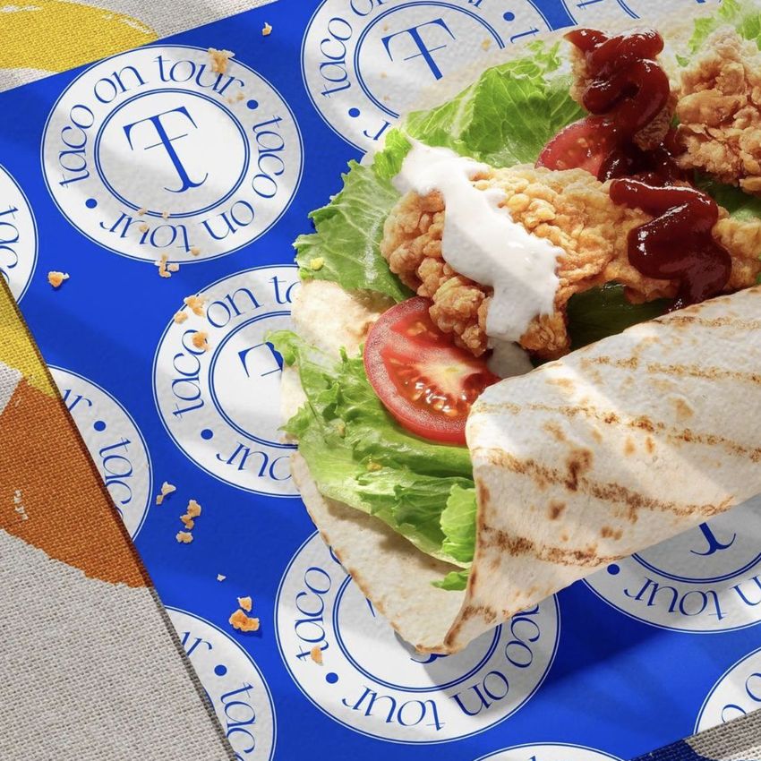 Food safe paper mockup featuring a tortilla wrap with fried chicken, lettuce, and tomato on blue patterned wrapping paper.