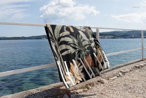 PSD mockup of a waffle beach towel featuring a botanical design, displayed on a seaside railing with water in the background.