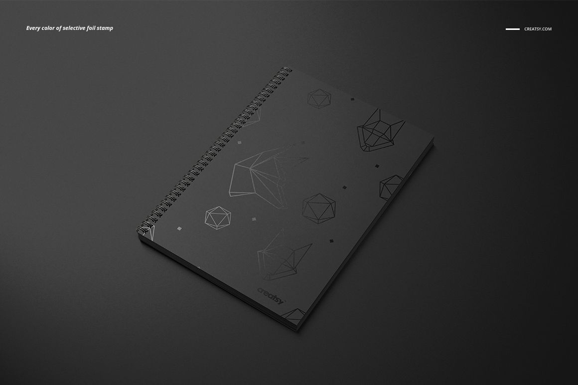 Black A4 notebook mockup with square holes and wire binding, geometric shapes on the cover, placed on dark surface.