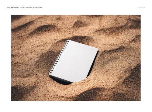 Top view of a spiral-bound planner mockup with a plain white cover resting on textured sand outdoors.