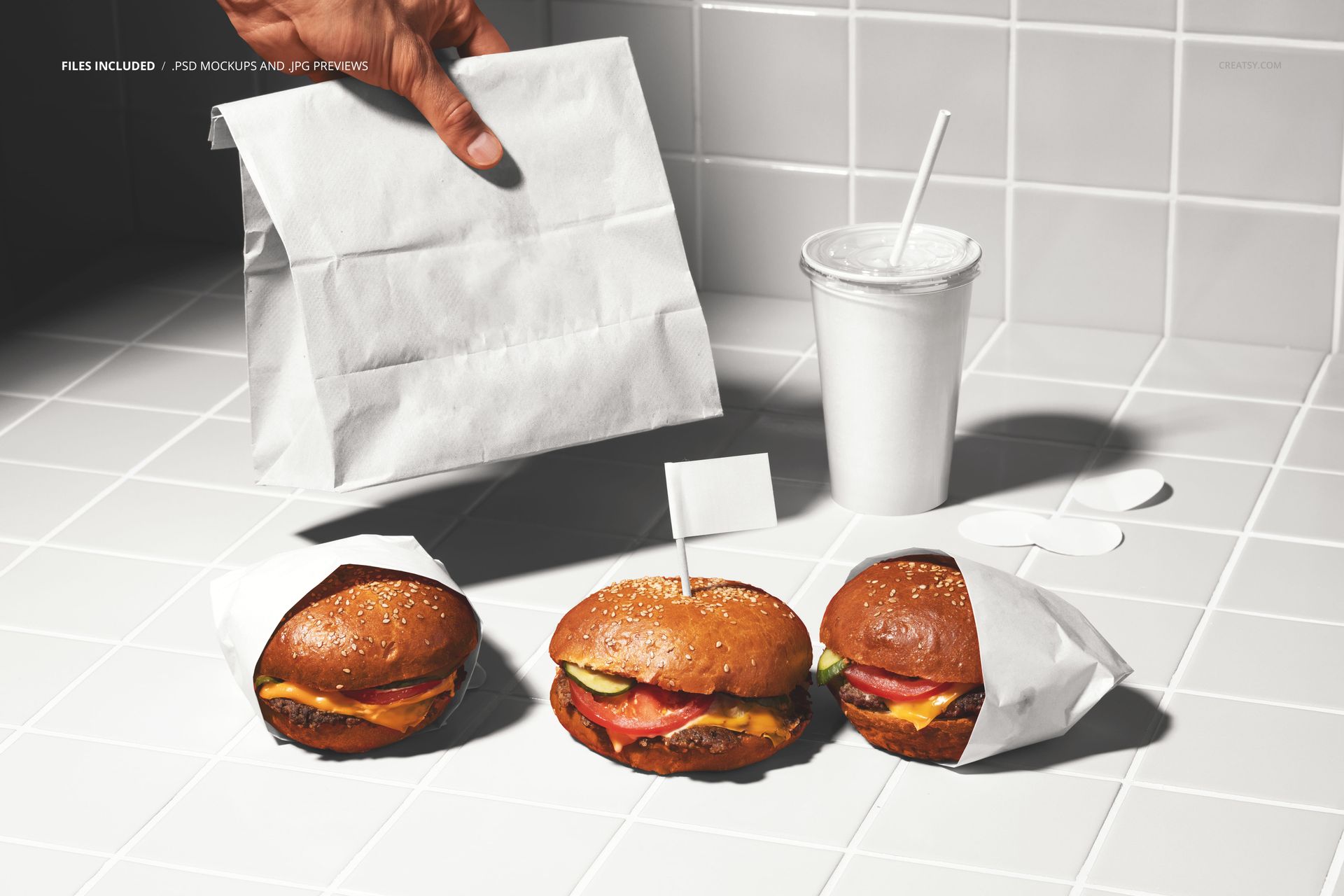 PSD mockup showing burgers in paper sleeves, a paper bag, and a disposable cup on a clean white tile background.